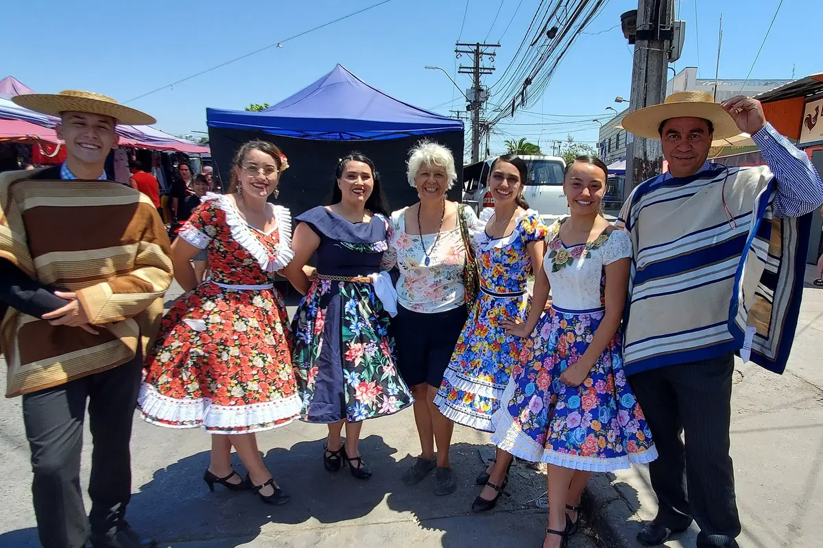 Two men in straw hats and striped ponchos and three women in flowered full-skirted dresses, in traditional cueca dress on a Chilean street